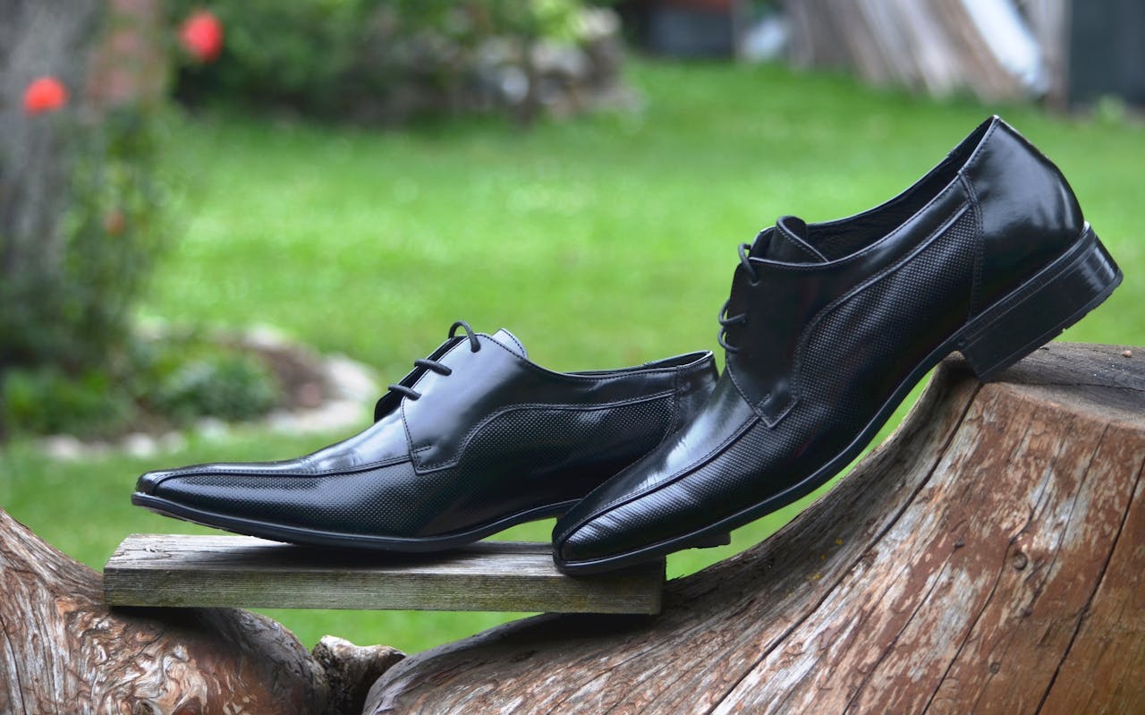 about-img Stylish black leather shoes displayed elegantly on a wooden log outdoors.