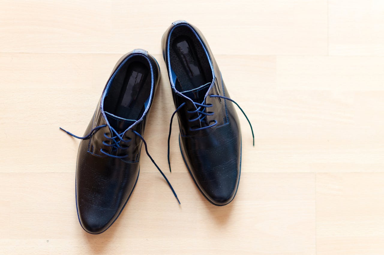 hero-img-01 Pair of stylish black leather shoes with blue laces on a wooden floor.