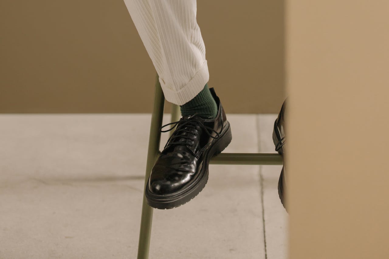 Close-up of elegant black leather shoes paired with white pants, showcasing a chic and modern style.