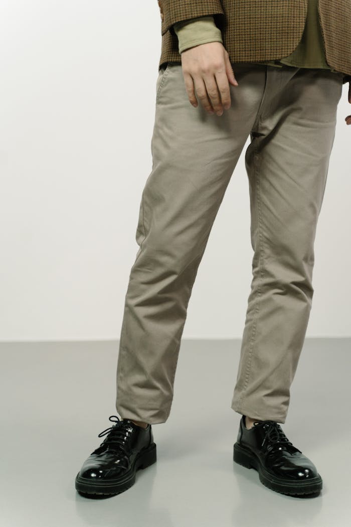 gallery-6 Elegant men's fashion showcasing shiny shoes and tailored trousers in a minimal setting.
